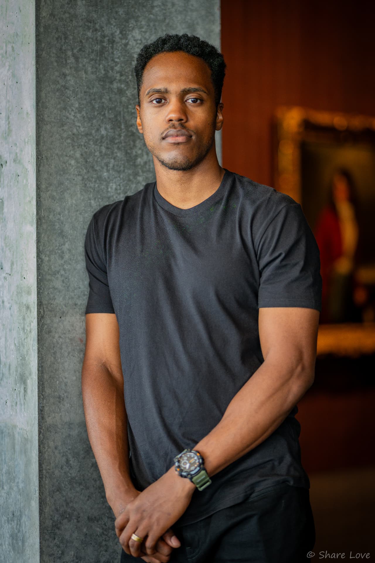 Tash Jordan leaning against a concrete wall in a black tee