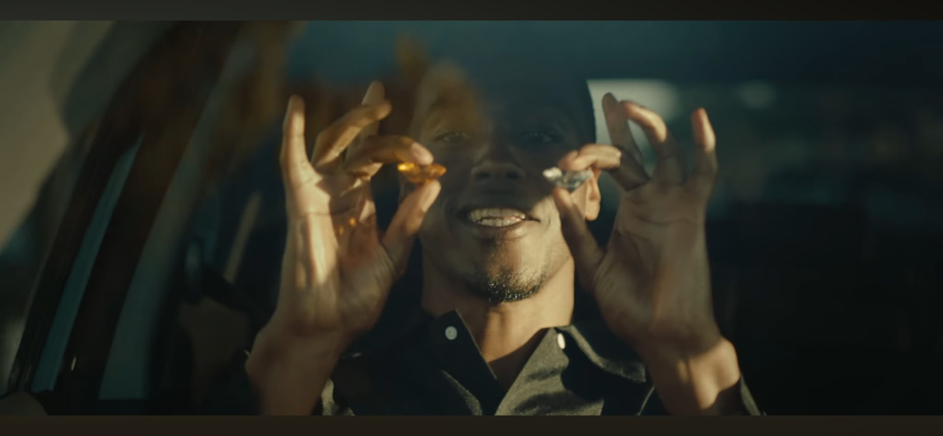 Tash Jordan smiling behind a car window holding jewels in a scene from The Deal